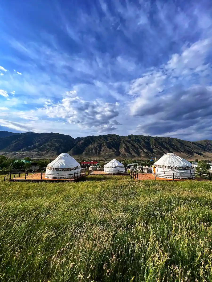 Row of traditional white yurts in a green valley in Kolsai with mountains behind
